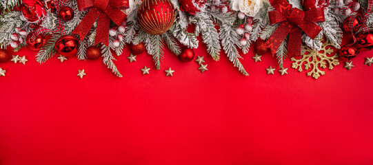 Wall Mural - christmas background with snowy pine branches, red baubles, bells, and festive flowers on a red surf