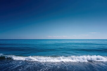 Wall Mural - Gentle ocean waves lap against a serene deep blue water under a clear sky, creating a peaceful atmosphere at a quiet seaside location