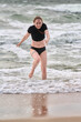 © TRAVELARIUM - Young woman in black activewear playfully runs from baltic sea waves. Overcast sky and rushing water create energetic coastal scene. Natural tones dominate inspiring image