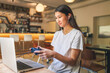 © aerogondo - Young Asian woman enjoys gaming while sitting at a cafe with a laptop and game controller