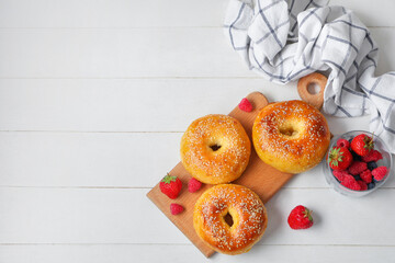 Wall Mural - Board with tasty bagels and fresh berries on white wooden background