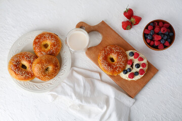 Wall Mural - Wooden board and plate of tasty bagels with berries on white background