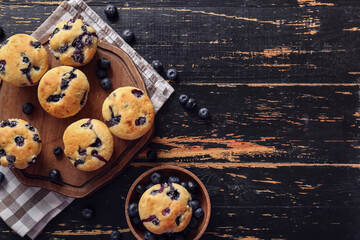 Wall Mural - Napkin, wooden tray and tasty blueberry muffins on black wooden background