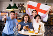 © JackF - Company of young adult emotional fans supporting English team with state flag while resting in sports bar with beer