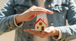 © ADD PHOTO - Hands holding small house model with red roof, symbolizing home protection, security, and real estate investment, with warm and caring atmosphere