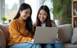 © wang - Two asian young woman happy smiling and using computer laptop on couch in living room at home. High quality