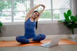 © Pang - A young woman practicing yoga indoors on an exercise mat, using a laptop for online training, symbolizing health, strength, and wellbeing.