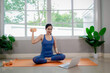 © Pang - A young woman practicing yoga indoors on an exercise mat, using a laptop for online training, symbolizing health, strength, and wellbeing.