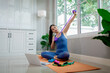 © Pang - A young woman practicing yoga indoors on an exercise mat, using a laptop for online training, symbolizing health, strength, and wellbeing.