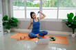© Pang - A young woman practicing yoga indoors on an exercise mat, using a laptop for online training, symbolizing health, strength, and wellbeing.
