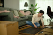 © saltdium - Indoor lifestyle scene of a man sitting cross-legged, unpacking furniture parts and arranging tools for assembly