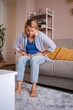 © Jelena - Woman experiencing abdominal pain while sitting on sofa at home
