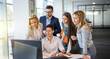 © Bojan - Business people gathered around young colleague at computer discussing potential development results and generating ideas together