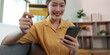 © Natee Meepian - Online Shopping. Happy woman holding credit card and smartphone while shopping online.