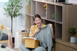 © Natee Meepian - Online Shopping. Young woman unboxing a sweater while smiling at home.