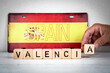 Hand arranging wooden letter blocks spelling Valencia in front of Spanish flag license plate with word Spain