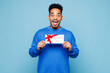 © ViDi Studio - Young surprised man of African American ethnicity wear sweatshirt casual clothes hold gift certificate coupon voucher card for store isolated on plain pastel light blue background. Lifestyle concept.