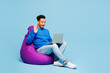© ViDi Studio - Full body young IT man wear sweatshirt casual clothes sit in bag chair hold use work on laptop pc computer waving hand isolated on plain pastel light blue background studio portrait Lifestyle concept