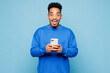 © ViDi Studio - Young shocked man of African American ethnicity wear sweatshirt casual clothes hold in hand use mobile cell phone isolated on plain pastel light blue cyan background studio portrait Lifestyle concept