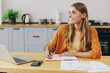 © ViDi Studio - Young minded housewife IT woman wear orange shirt casual clothes hold use work on laptop pc computer write down in notebook sit at table in light kitchen at home alone. Lifestyle cooking food concept.