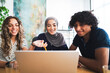 © Studio Marmellata - Three diverse young adults, two women and one man, are collaborating around a laptop. One woman points at the screen with a pencil, all smiling.