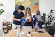 © Studio Marmellata - A diverse group of three young adults, including a man and two women, one wearing a hijab, collaborate around a table. They are smiling, discussing content in a blue notebook