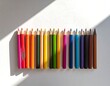 © Armaya - Colorful pencils arranged in a row, sunlight casts shadows