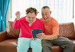 © offsuperphoto - A man with down syndrome and senior man sharing an excited moment together while looking at a tablet on a sofa