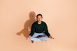 © deagreez - Young man seated in a meditative pose on beige background showcasing calmness and focus, ideal for mindfulness and wellness themes