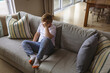 © wavebreak3 - Child boy sitting on light grey sofa with striped cushions at home living room rubbing eyes
