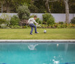 © wavebreak3 - School-age boy dribbling black-and-white soccer ball on manicured lawn beside swimming pool