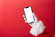 © seba - Christmas concept, Santa Claus hand holding a smartphone with blank screen with copy space on red background