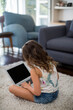 © wavebreak3 - Female child wearing denim shorts sitting on rug in sunlit living room using laptop near sofa
