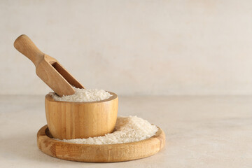 Wall Mural - Wooden tray and bowl of raw rice with scoop on light background