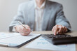 © Garun Studios - Businessman using calculator and reviewing financial reports for accounting, tax, and business analysis in the office.