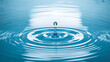 © zawak - A water droplet creates ripples on a calm blue surface, capturing the moment of impact and reflection.