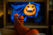 © Nanci - Halloween streaming at home concept with orange striped socks, cozy living room atmosphere and blurred scary pumpkin decor for autumn lifestyle.
