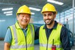 © Pixels Hunter - Two smiling construction workers wearing safety vests and helmets standing together in a warehouse with bright lighting in the background.