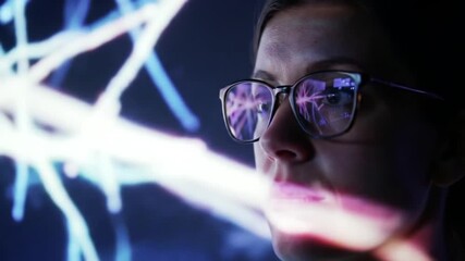 Close-Up Of A Focused Woman With Glasses Analyzing A Futuristic Data Projection. Light Reflects On Her Face