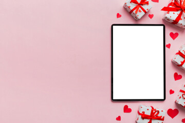 Wall Mural - Top view of digital tablet with gift boxes and hearts on colorful background. Tablet with black screen with Holiday decorations gift box top view