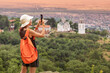 © EdNurg - Female hiker taking pictures of a church on a hill overlooking a small town of Vrsac, Serbia during a colorful sunset