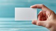 © Breken - A hand holds a blank white business card against a teal wooden background (1)