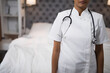© wavebreak3 - Female nurse wearing white uniform and stethoscope standing in bedroom by unmade bed with lit lamp