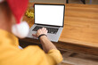 © wavebreak3 - Mature adult man typing on laptop at home office table with tinsel, Santa hat, copy space