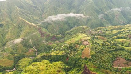 Wall Mural - Cinematic aerial view of lush green mountains with winding roads, farms, and misty clouds, perfect for nature, travel, agriculture, and landscape projects