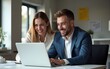 © Riley - Two business people using a laptop together in an office. High quality