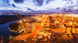 © AmazingAerialAgency - Oakland, United States - 11 May 2020: Aerial view of the Port of Oakland glows with warm light against the cool blues of twilight, the cranes and cargo ships standing as monuments to global trade.