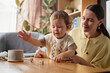 © Seventyfour - Caucasian young mother watching toddler playing with wooden dreidels on table during Hanukkah celebration, both sitting together in cozy home setting, mother smiling gently