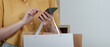 © Natee Meepian - Shopping Experience. Close-up of woman using smartphone while holding shopping bag.