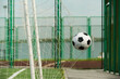 © Mediaphotos - Soccer ball hitting net of outdoor goal on sports field, capturing moment of scoring during game, green fence and running track visible in background, no people present